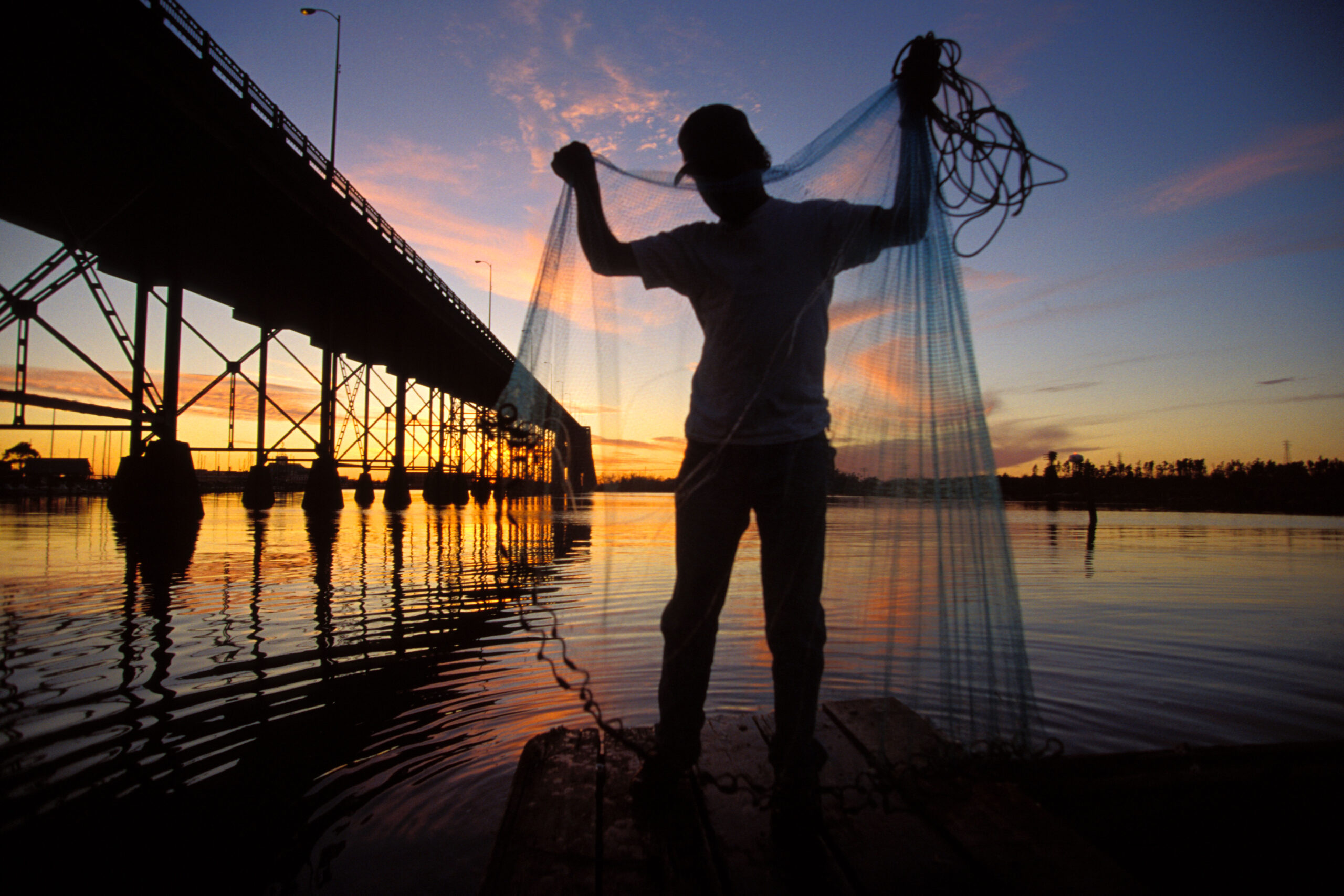 Fisherman getting his net together on the dock under the bridge in Lake Charles Louisiana