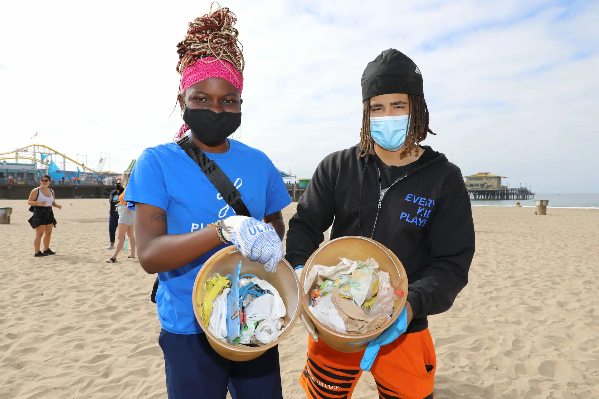 two volunteers hold buckets of trash on beach