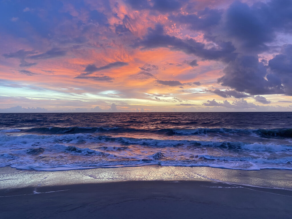 An incredible sunsetting across the ocean. The sky is streaked with pink, purple and gold.