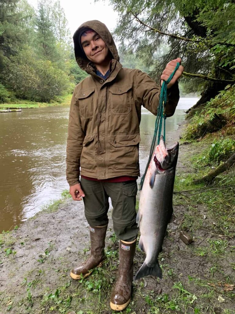 Salmon catching: K’alaagáa Íihlangaa (Nathaniel) Blake harvesting salmon along a river in Dzantik'i Héeni (Juneau), Alaska.