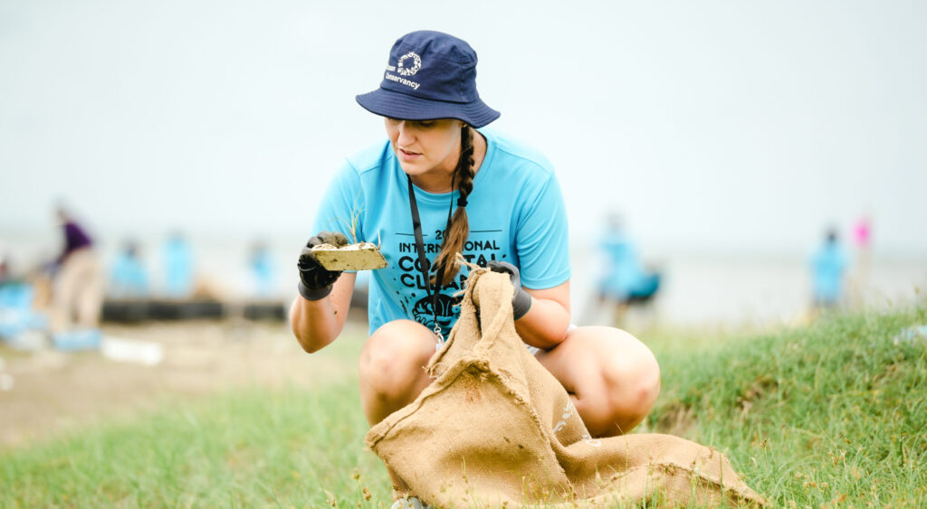Sarah Weller clad in Ocean Conservancy's International Coastal Cleanup gear picks up debris on the coast in Vietnam